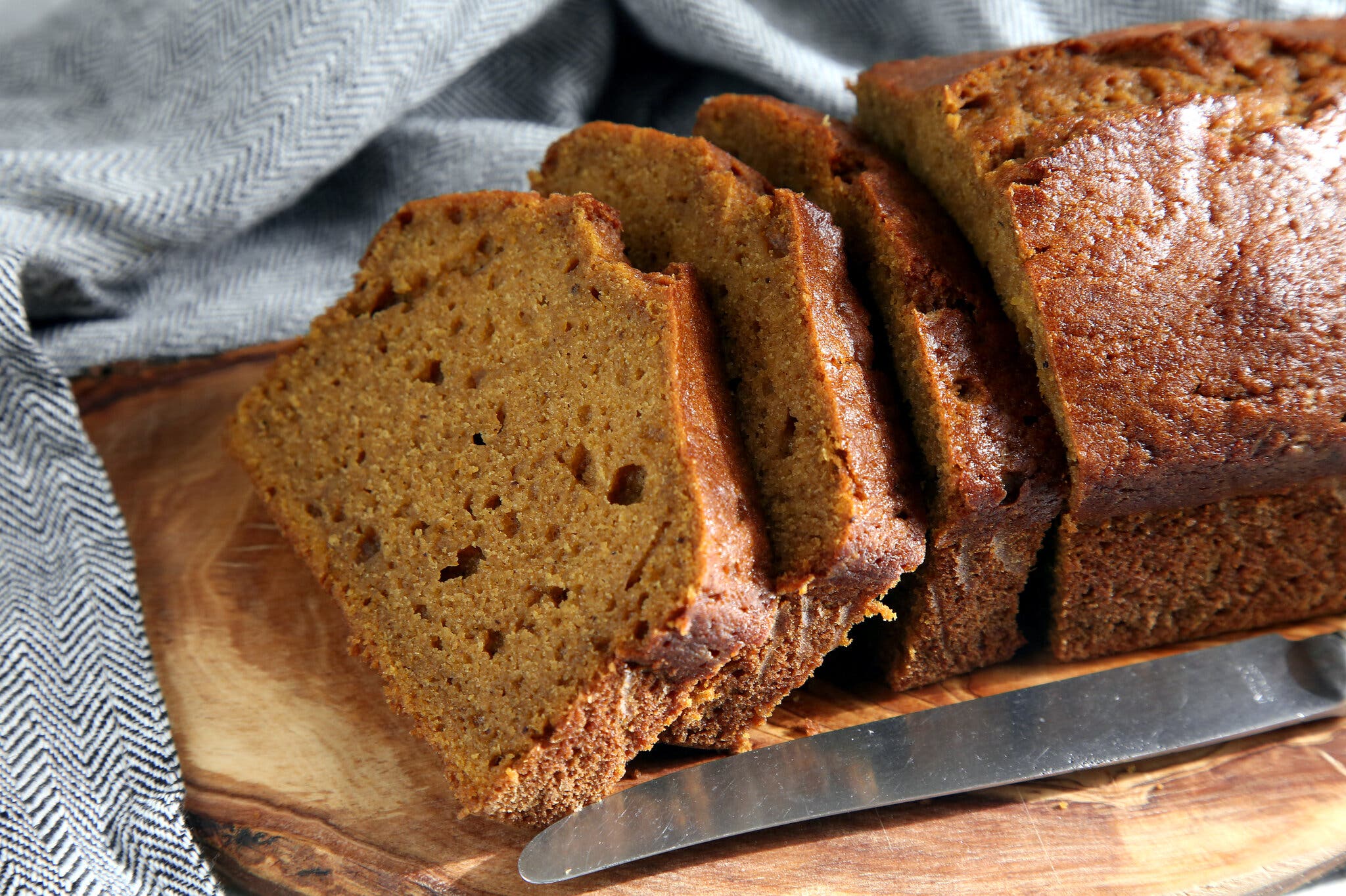A loaf of pumpkin bread photographed from the side with three slices cut from one end.