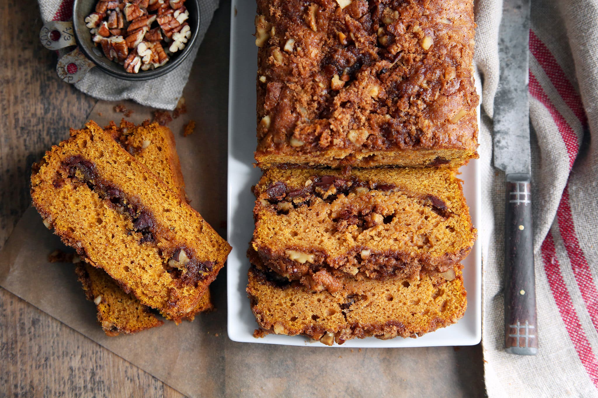 A loaf of pumpkin bread with chocolate chip streusel sits on a dish, with several pieces sliced off and lying on their sides next to it.