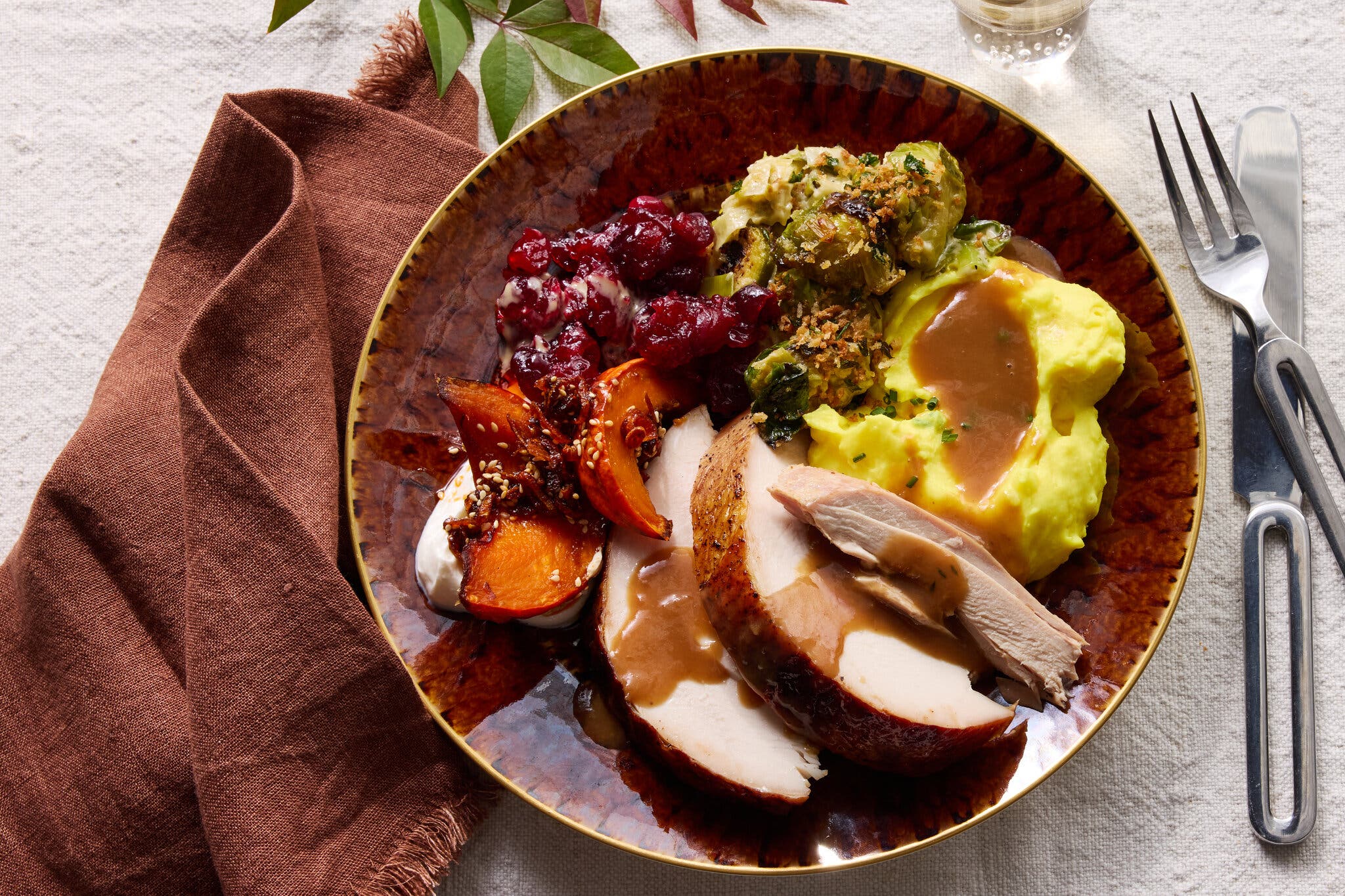A single plate of Thanksgiving-style food, including sliced turkey with gravy, cranberry sauce, yellow mashed potatoes, brussels sprouts and a sweet potato with cream.