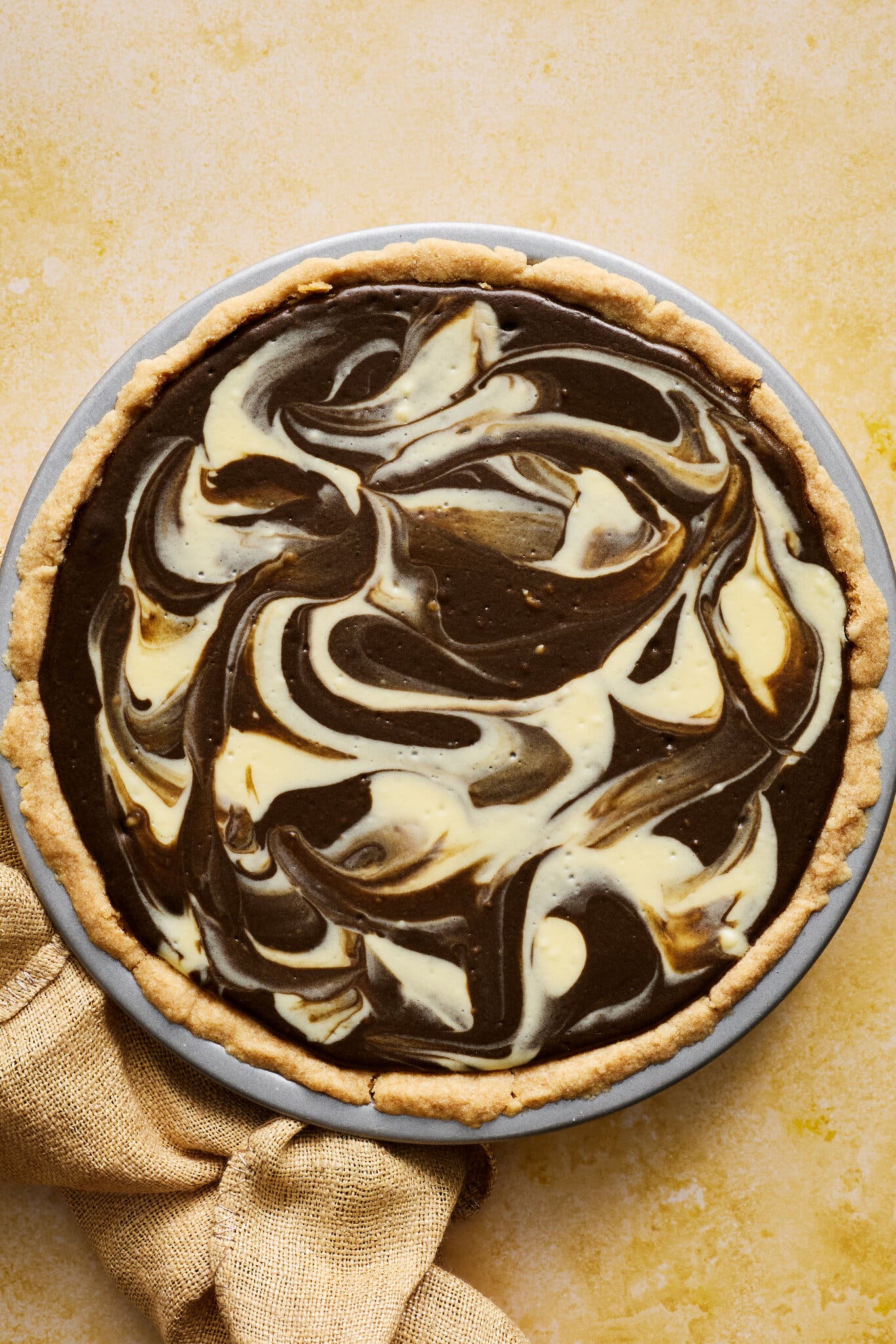 An overhead shot of a pie with marbled swirls of dark and light custard sitting on a light yellow background.
