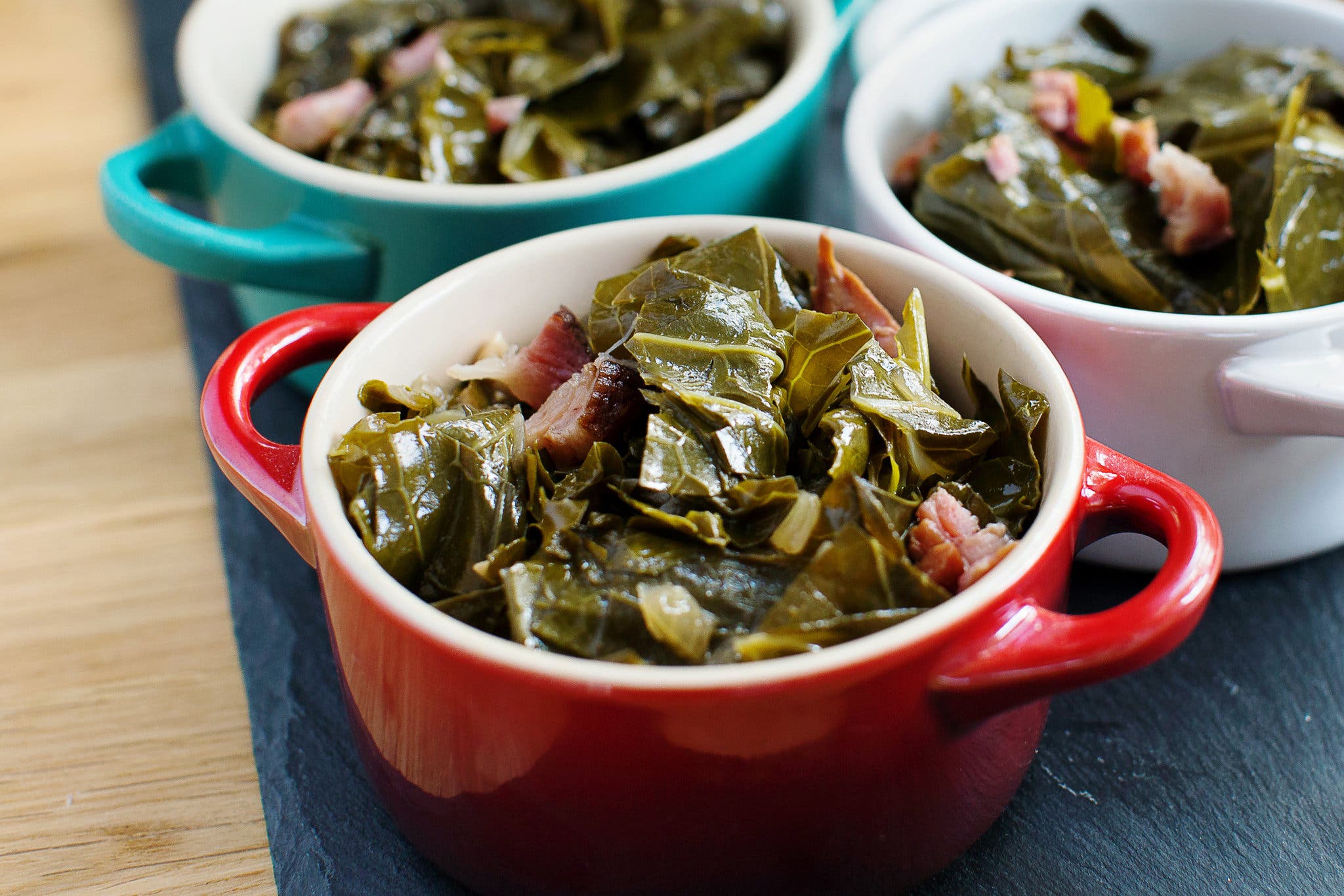Three bowls of collard greens with ham, shown from the side.