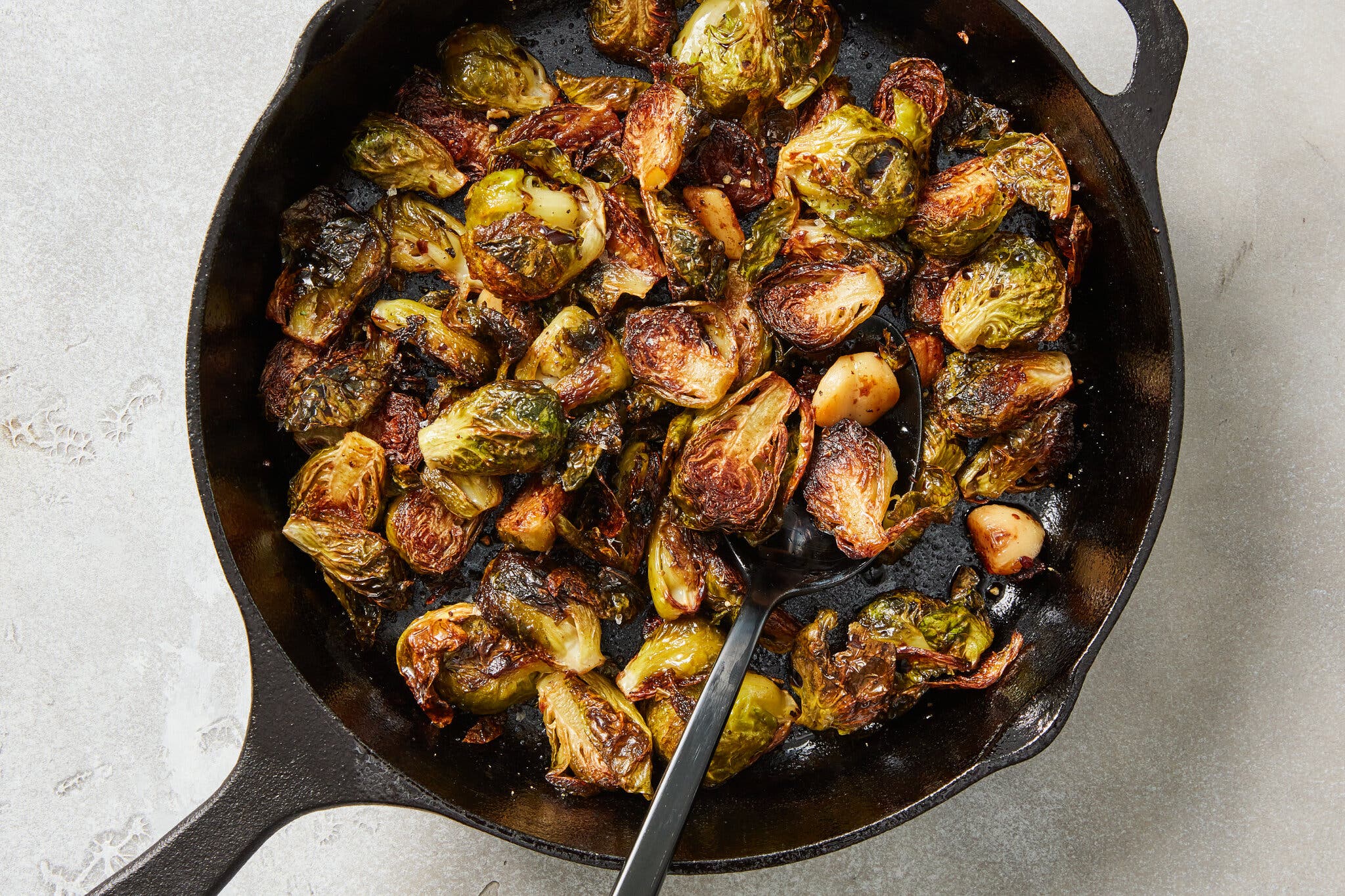 Roasted brussels sprouts and garlic fill a black cast-iron skillet.