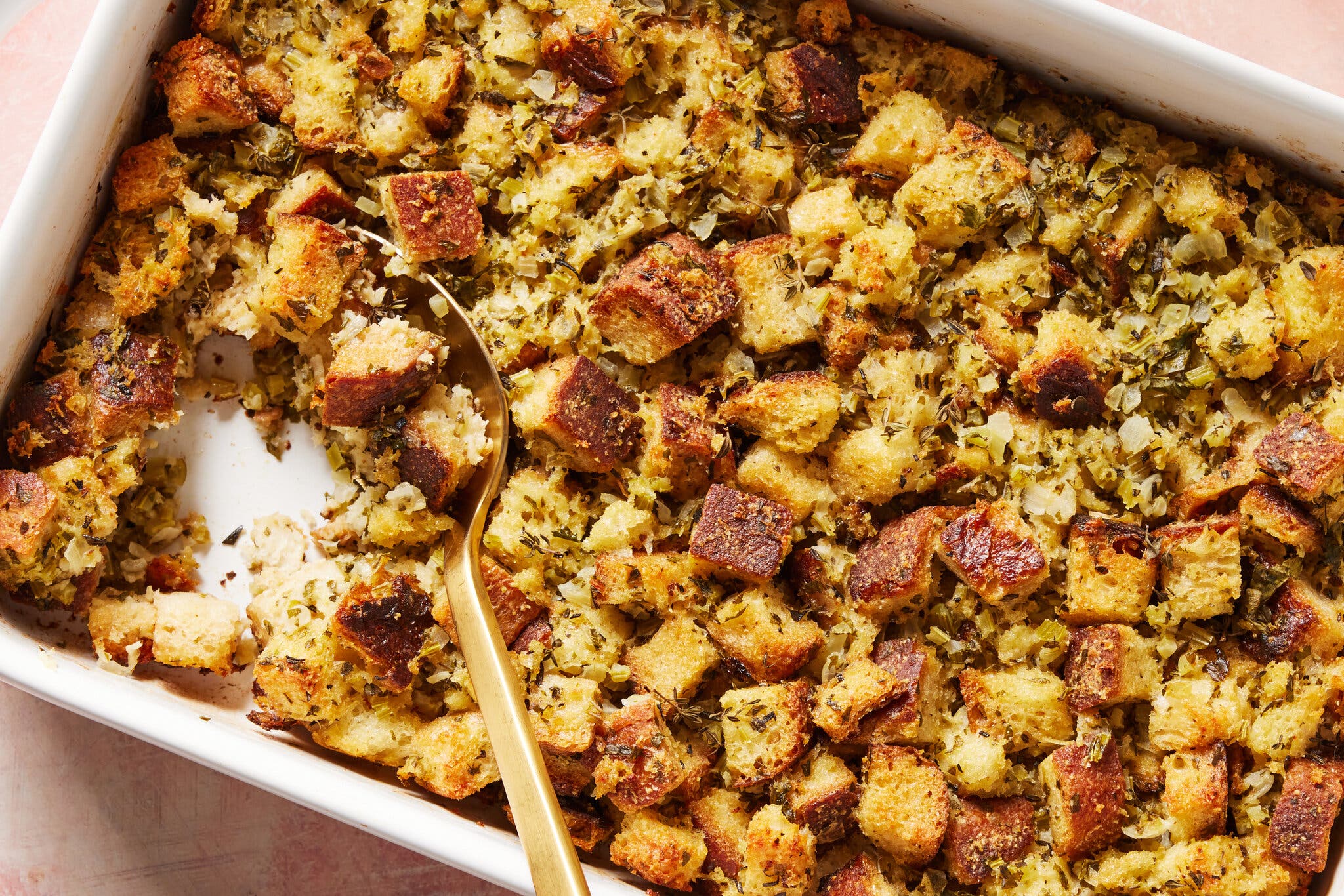 An overhead image of stuffing in a white baking dish. A scoop pulled out where a serving spoon now sits.