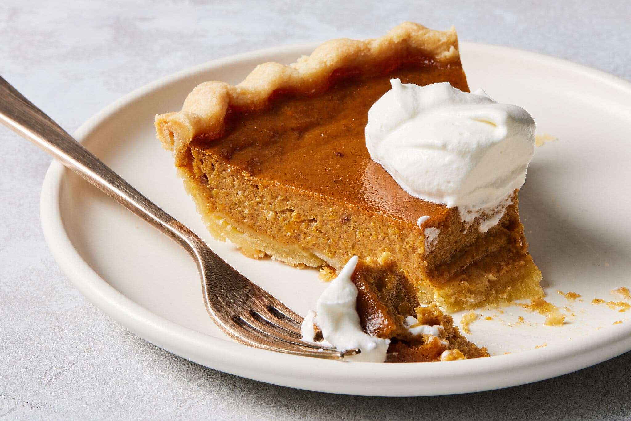 A slice of pumpkin pie topped with whipped cream and photographed from the side.