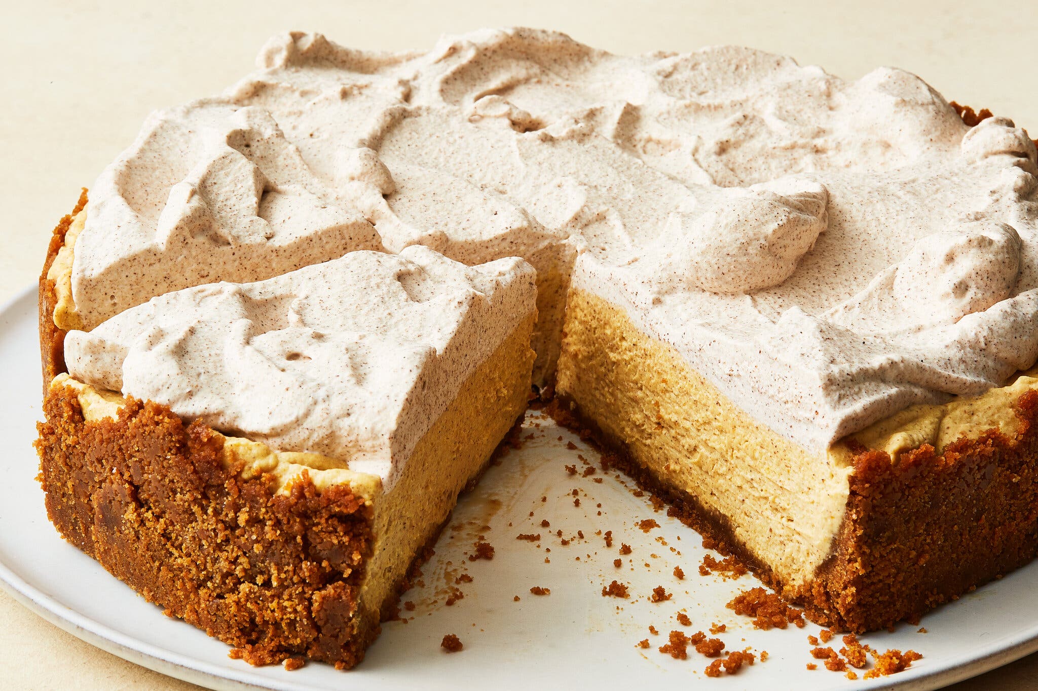 A lush cheesecake topped with whipped cream and a couple of slices removed is photographed from the side.