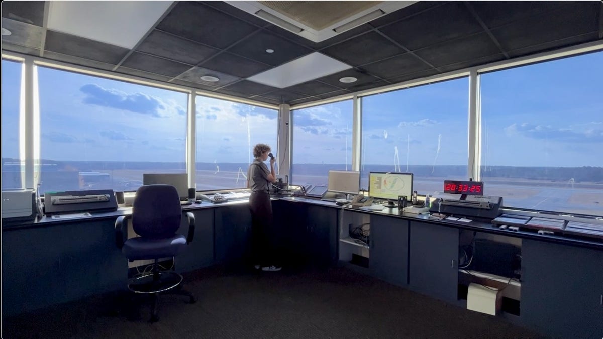 Student speaks into a radio inside the airport’s control tower with a clear view of the runway.