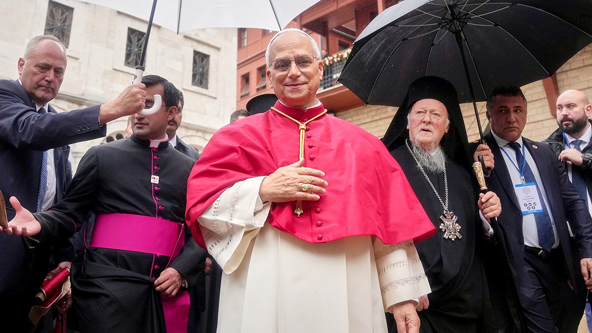 Pope Leo XIV and Ecumenical Patriarch Bartholomew I walk outdoors under umbrellas with aides during a rainy day in Istanbul.