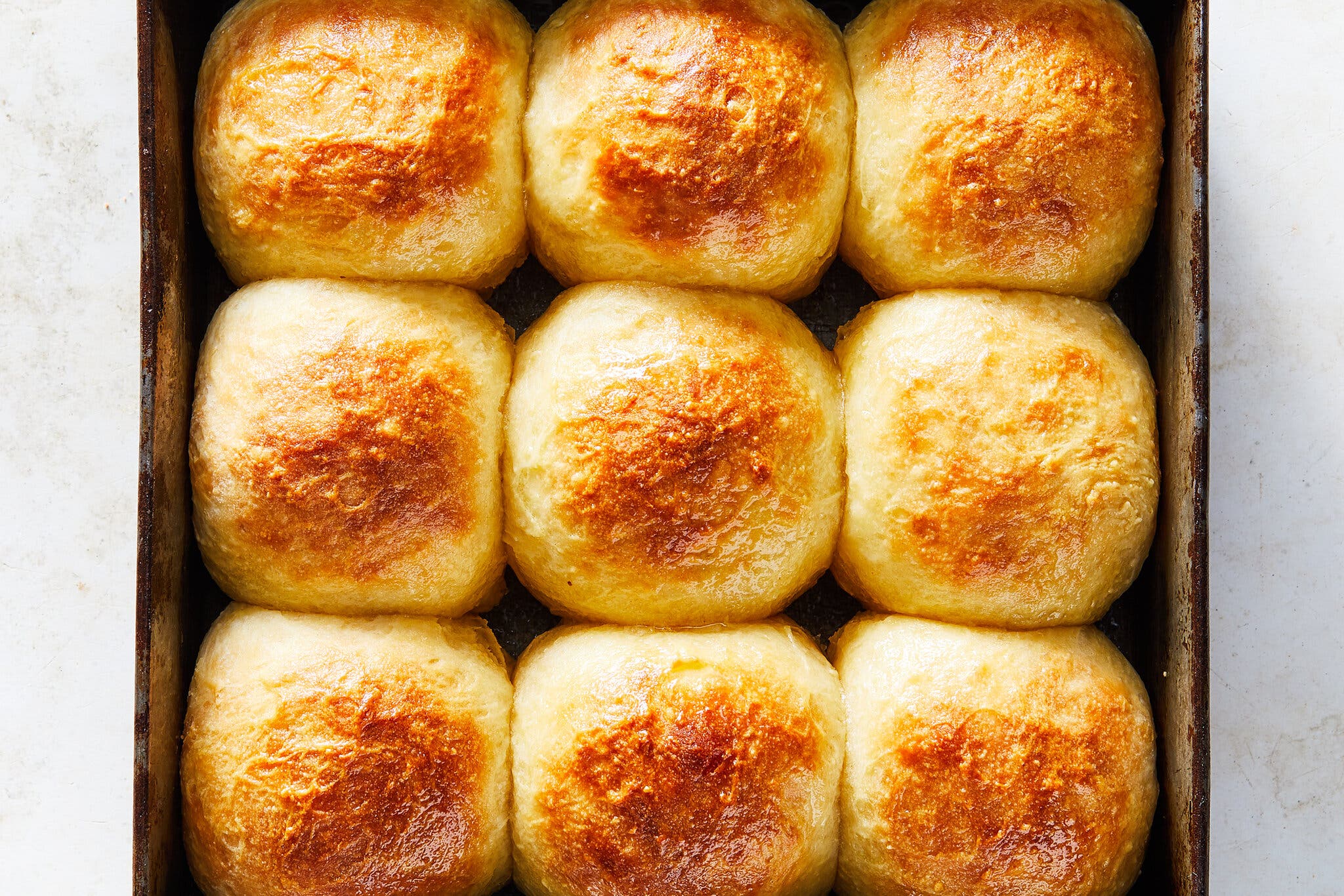 An overhead image of a square metal baking pan filled with nine browned dinner rolls.
