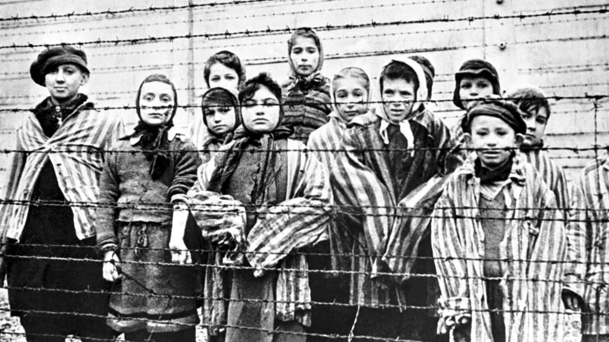 A group of child survivors behind a barbed wire fence at the Nazi concentration camp at Auschwitz-Birkenau in southern Poland, on the day of the camp’s liberation by the Red Army, 27th January 1945. Photo taken by Red Army photographer Captain Alexander Vorontsov during the making of a film about the liberation of the camp. The children were dressed in adult uniforms by the Russians. The children are (left to right): Tomy Schwarz (later Shacham), Miriam Ziegler, Paula Lebovics (front), Ruth Webber, Berta Weinhaber (later Bracha Katz), Erika Winter (later Dohan), Marta Weiss (later Wise), Eva Weiss (later Slonim), Gabor Hirsch (just visible behind Eva Weiss), Gabriel Neumann, Robert Schlesinger (later Shmuel Schelach), Eva Mozes Kor, and Miriam Mozes Zeiger.