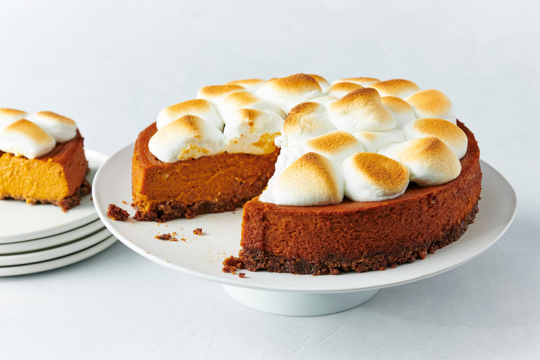 A sweet potato casserole pie with a cookie crust, on a cake stand. It’s topped with lightly browned marshmallows.