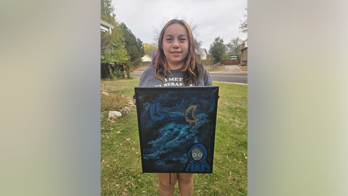 An image of Mia Corado holding up a painting with wings