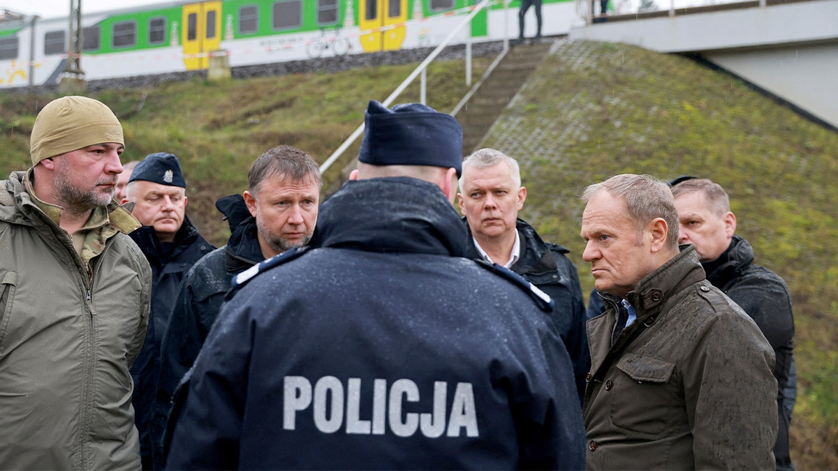 Donald Tusk surveys a railway site surrounded by officials and investigators after an explosion.