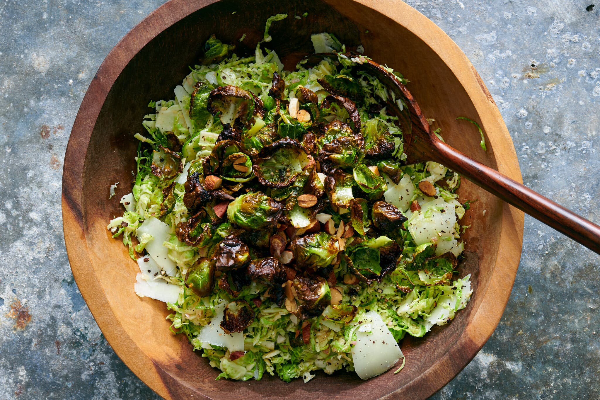 An overhead image of shredded brussels sprouts topped with nuts and dried fruit in a wooden bowl.