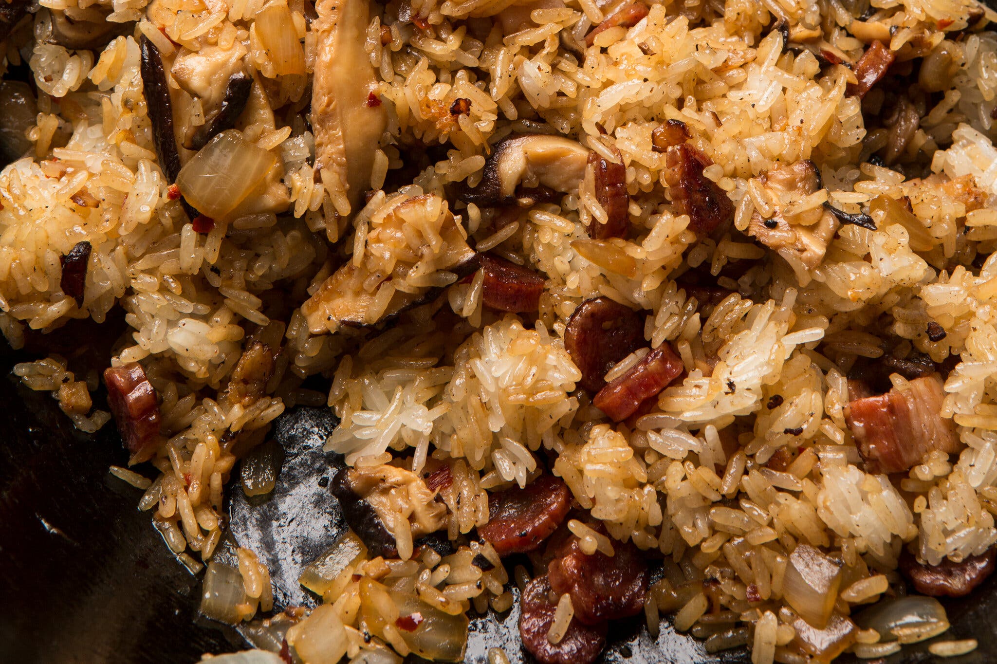 A close-up image of sticky rice with sliced Chinese sausage, onion and shiitake mushrooms.