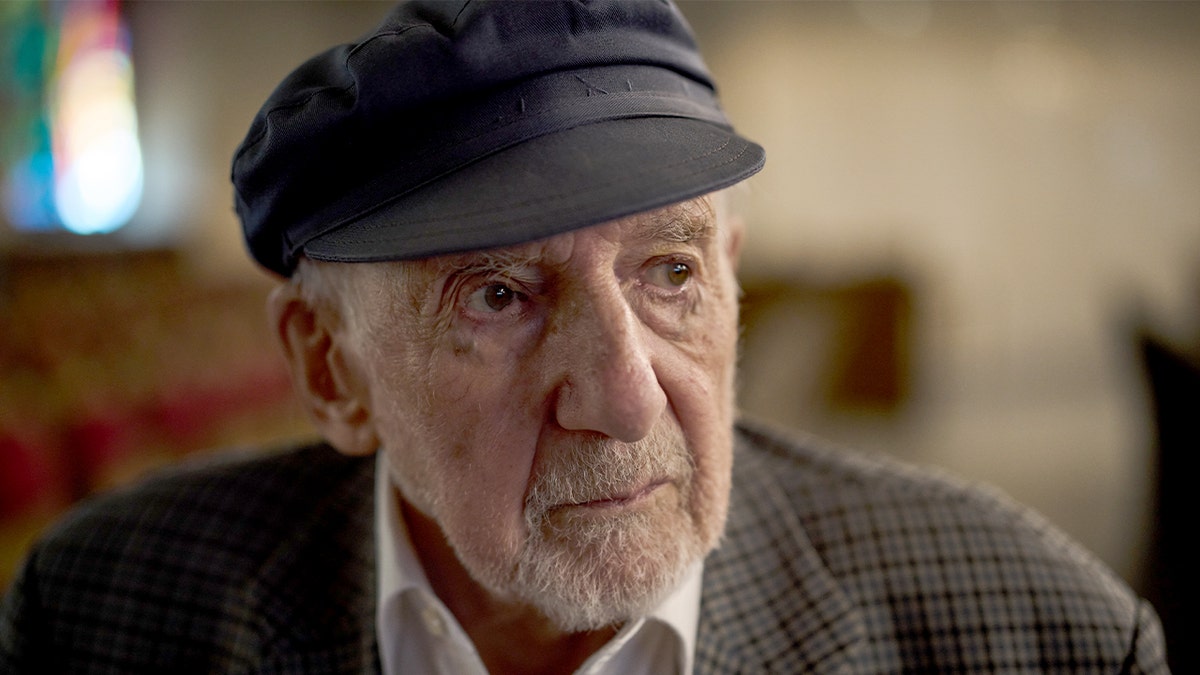 An elderly man stands inside a synagogue, preparing to commemorate a historic event tied to Jewish persecution.