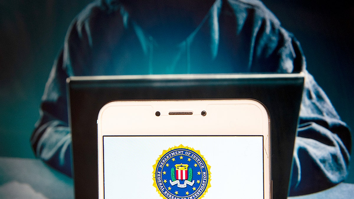 Hacker on a computer with a phone in front.