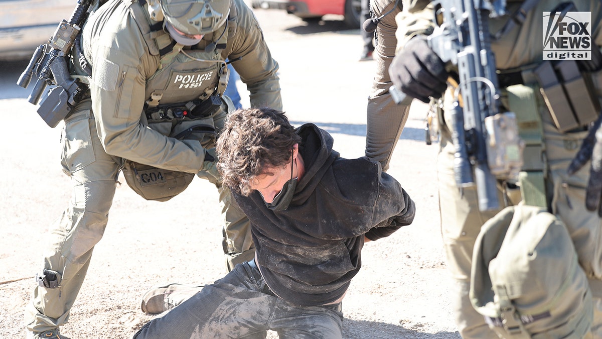 A man in a black sweatershirt is placed under arrest