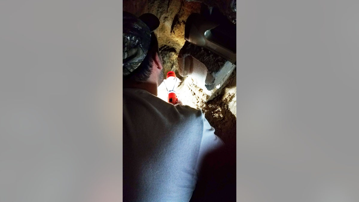 A shot over the shoulder as Chris Carroll leans into the hole he's dug with a light.