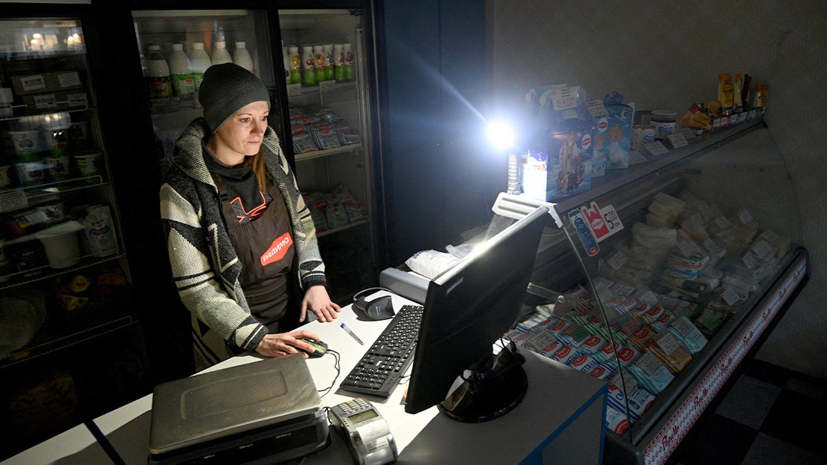 A shop illuminated by dim light as a vendor waits during a power outage in Lviv.