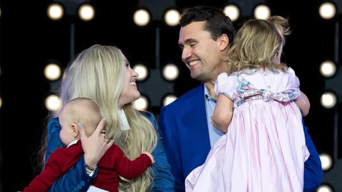 Charlie Kirk with family on Christmas, him and wife Erika smiling at each other, holding two kids