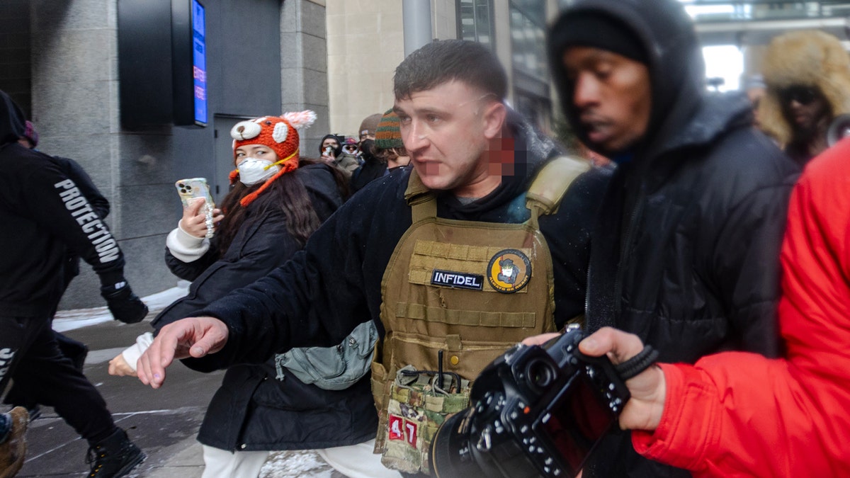 Jake Lang tries to walk away from protesters with blood on neck and mouth covered by blurring