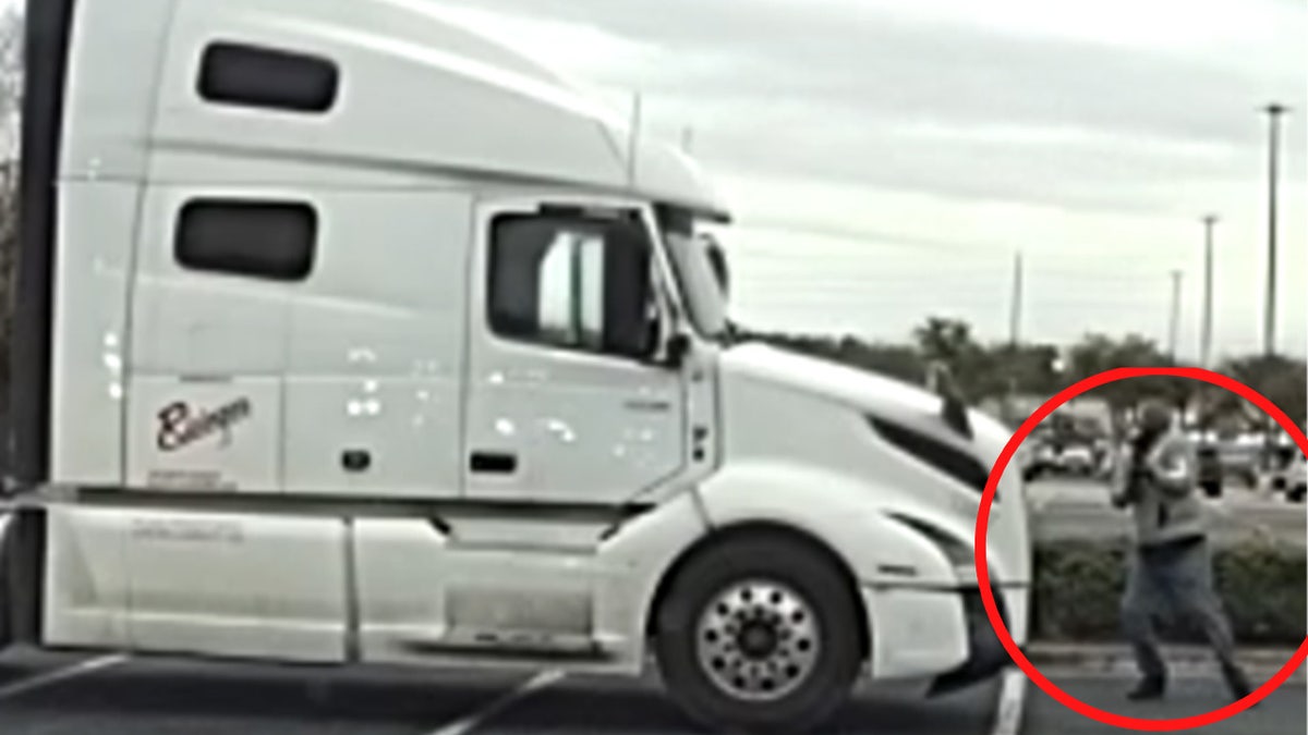 Surveillance image shows a white semi-truck parked in a shopping center lot as a man stands near the front of the vehicle, highlighted by a red circle