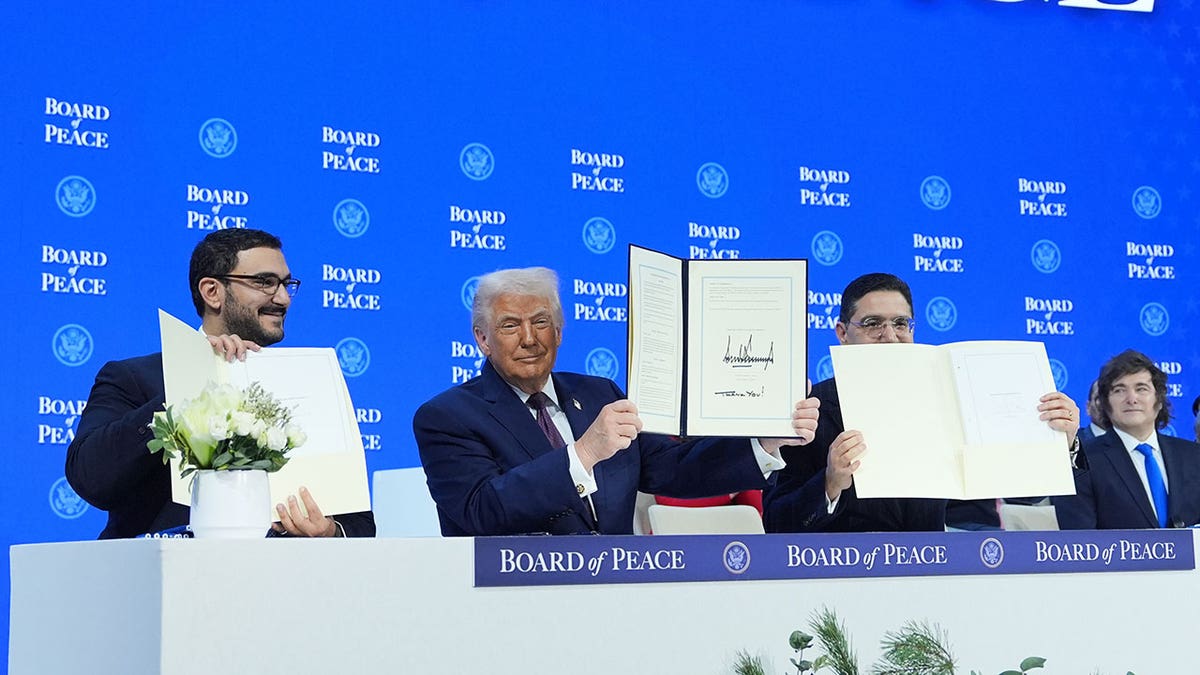 Donald Trump holding a signed document while standing between other individuals.