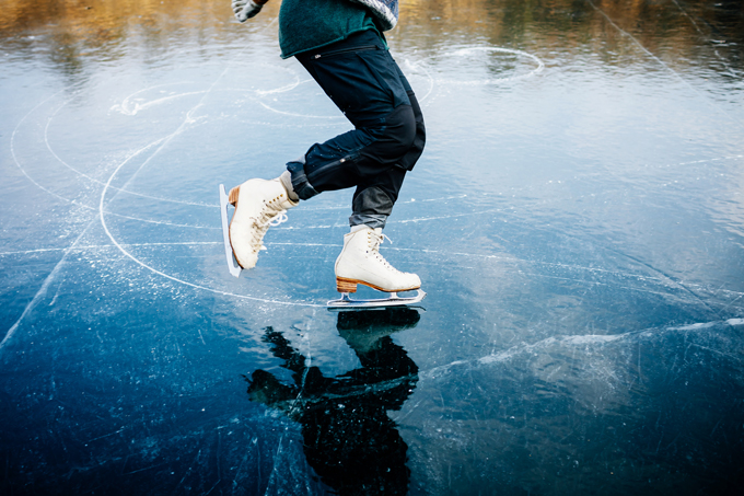 An person ice skates on a frozen lake. The ice appears black.