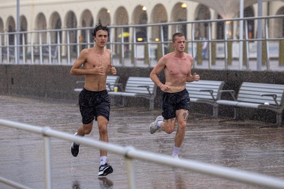 Runners make their way along the Bondi Beach promenade in pouring rain on Thursday evening.