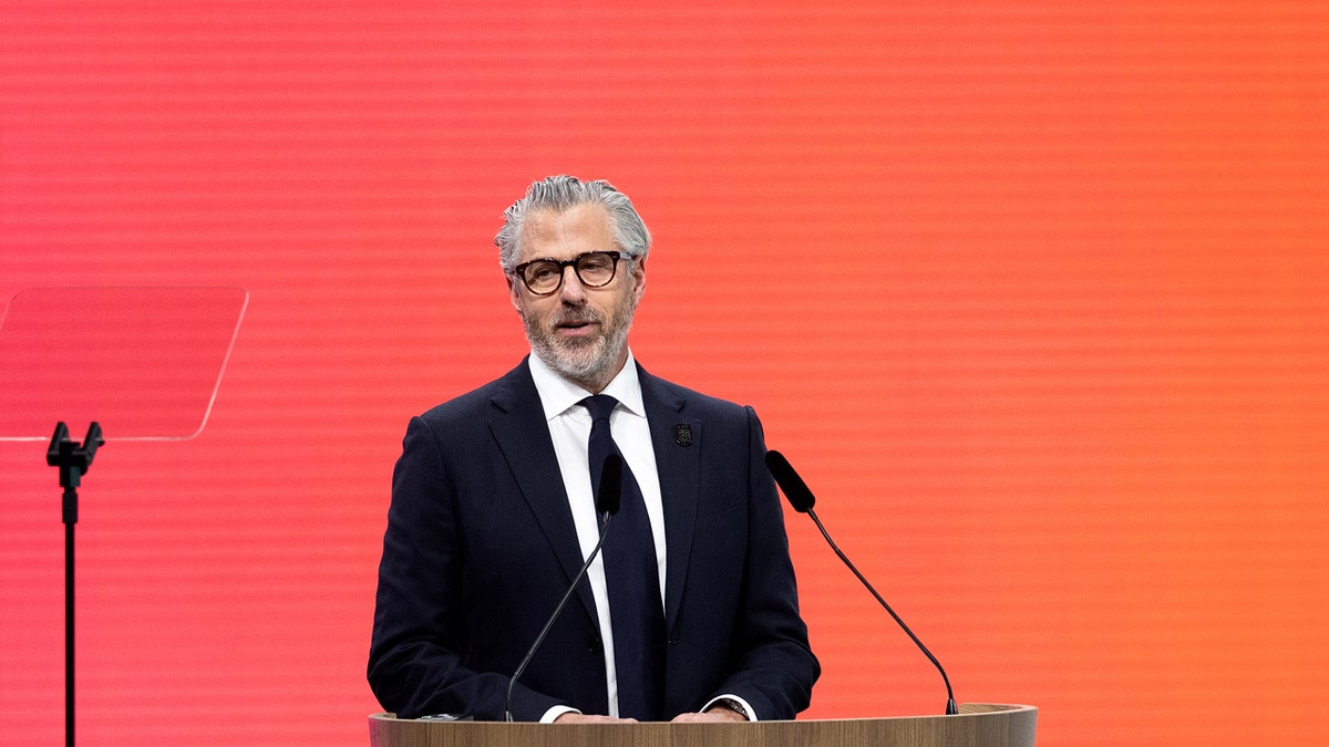 Casey Wasserman speaking at a podium during an indoor session.