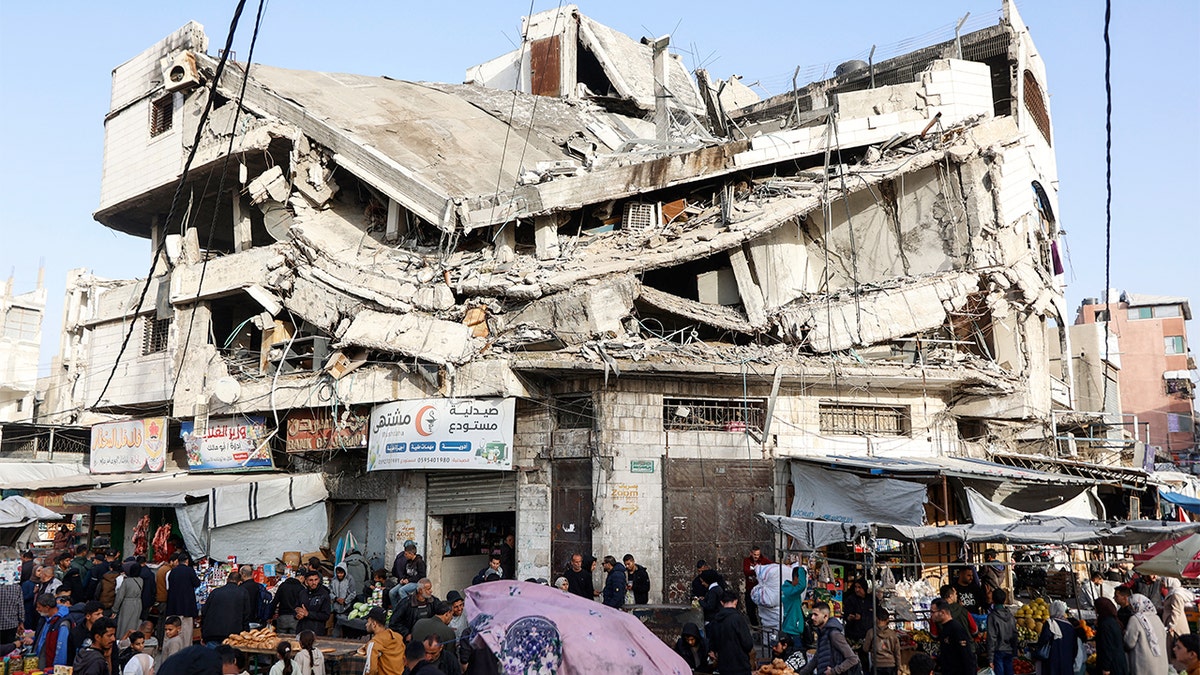 Shoppers purchase food at an open-air market set amid the rubble of a damaged building in Gaza City.
