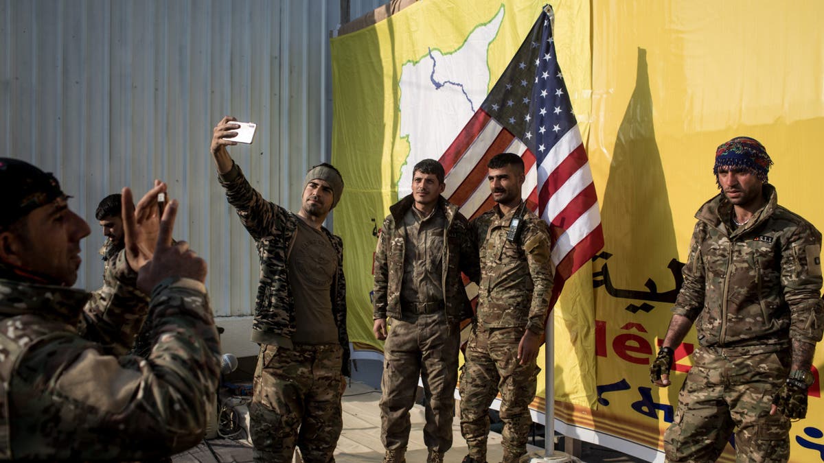 Syrian Democratic Forces (SDF) fighters pose for a photo with the American flag on stage after a SDF victory ceremony announcing the defeat of ISIL in Baghouz was held at Omer Oil Field on March 23, 2019 in Baghouz, Syria.Â