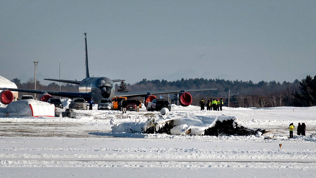 investigators stand before plane wreckage on a snow-covered runway