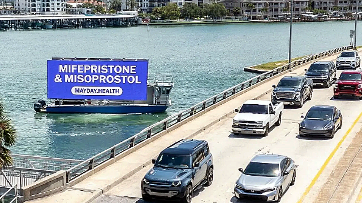 Traffic crosses a bridge in sunny Florida as a sign floats by on a skiff.