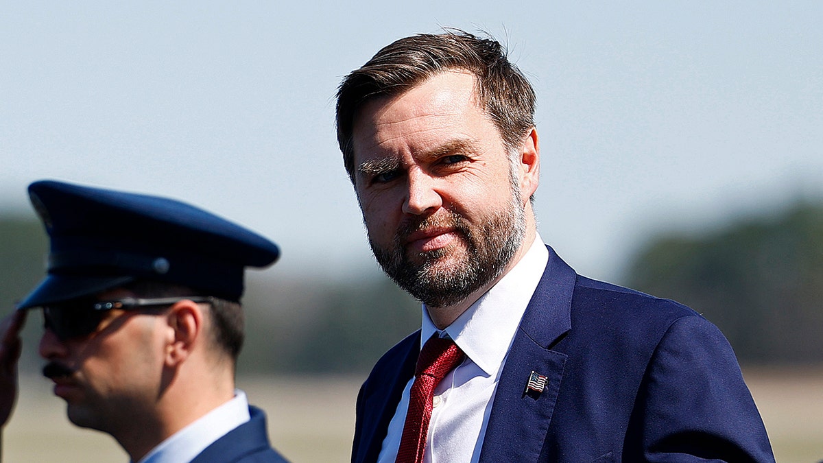 JD Vance looking at the camera next to a saluting soldier.