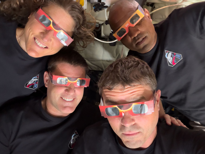 Four astronauts wear solar eclipse glasses.