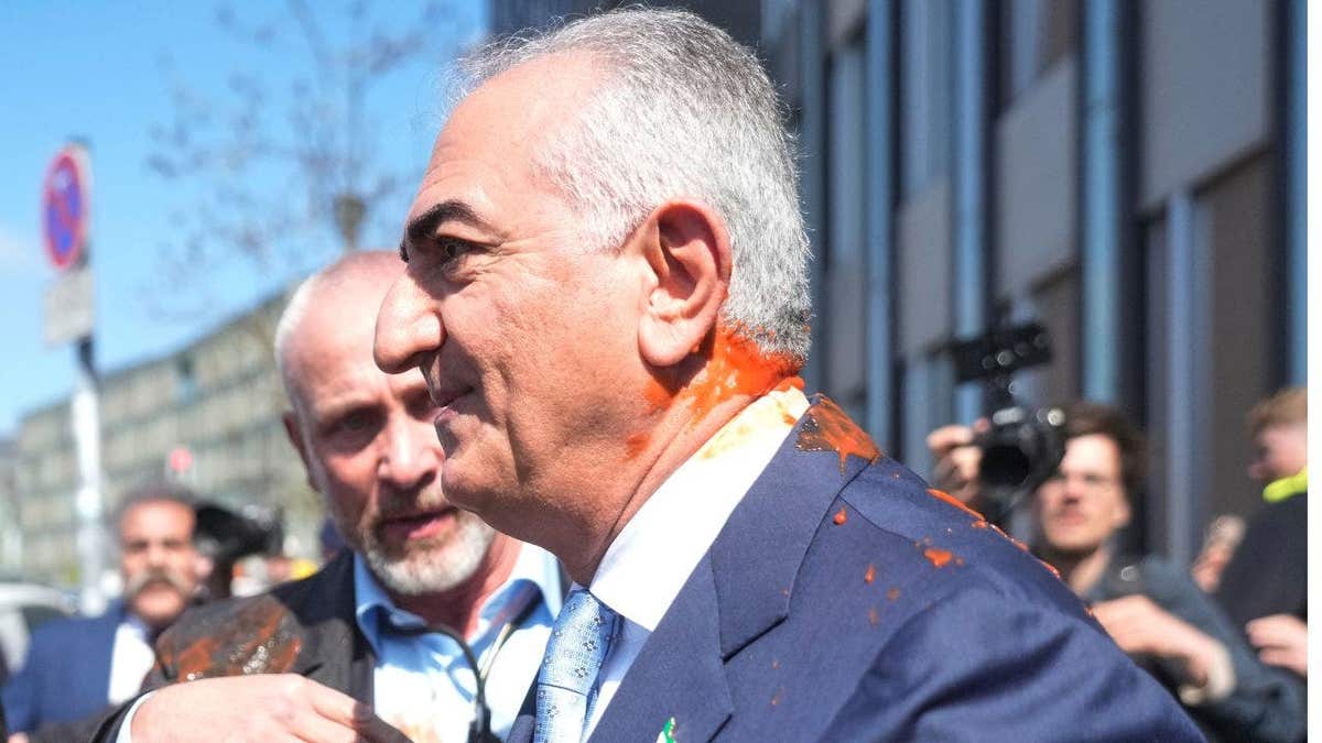 Reza Pahlavi looks out at a crowd while orange liquid runs down his neck and blue jacket
