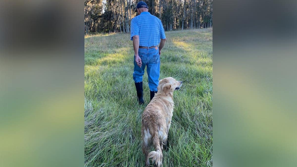 Bob Tebow walking through field with dog, seen from behind.