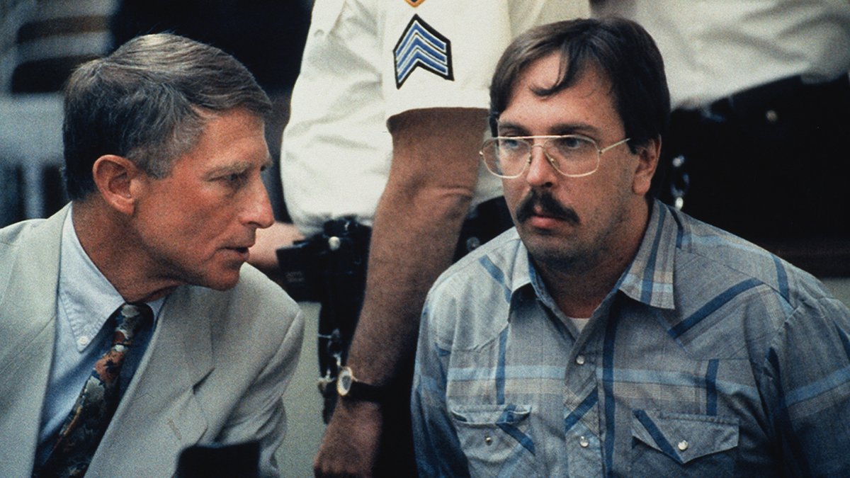Serial killer Joel Rifkin wearing a plaid shirt as he leans in to speak with his lawyer in court