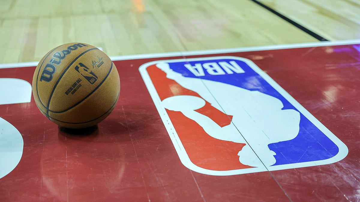 A basketball placed on the court next to an NBA logo during a break in a basketball game.