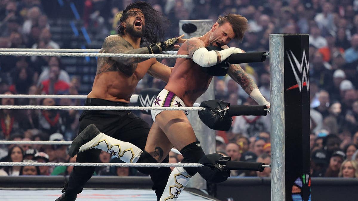 Roman Reigns shoving CM Punk into the ropes during a wrestling match at Allegiant Stadium