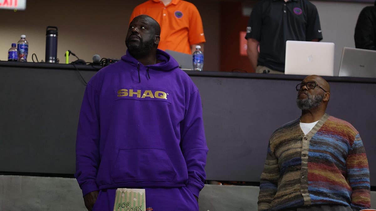 Shaquille O'Neal standing and honoring the flag at a basketball arena.
