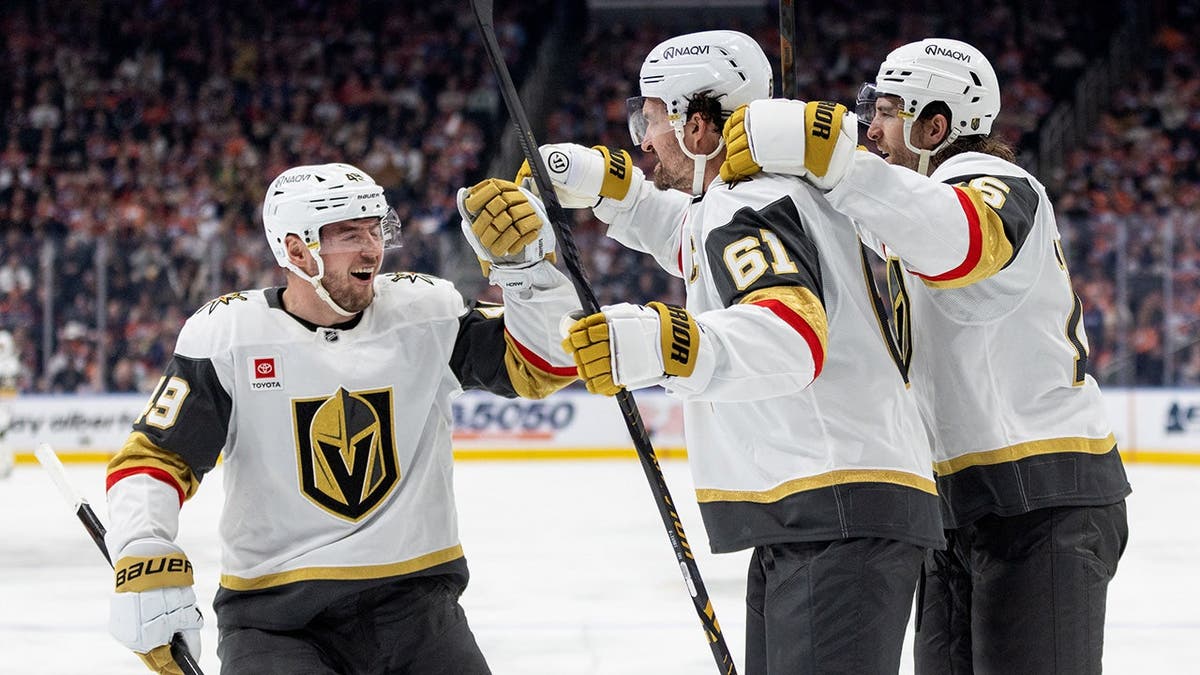 Vegas Golden Knights players Ivan Barbashev, Mark Stone, and Noah Hanifin celebrating a goal on ice.