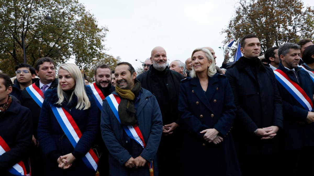 Marine Le Pen standing with deputies Sebastien Chenu and Jordan Bardella during a march in Paris
