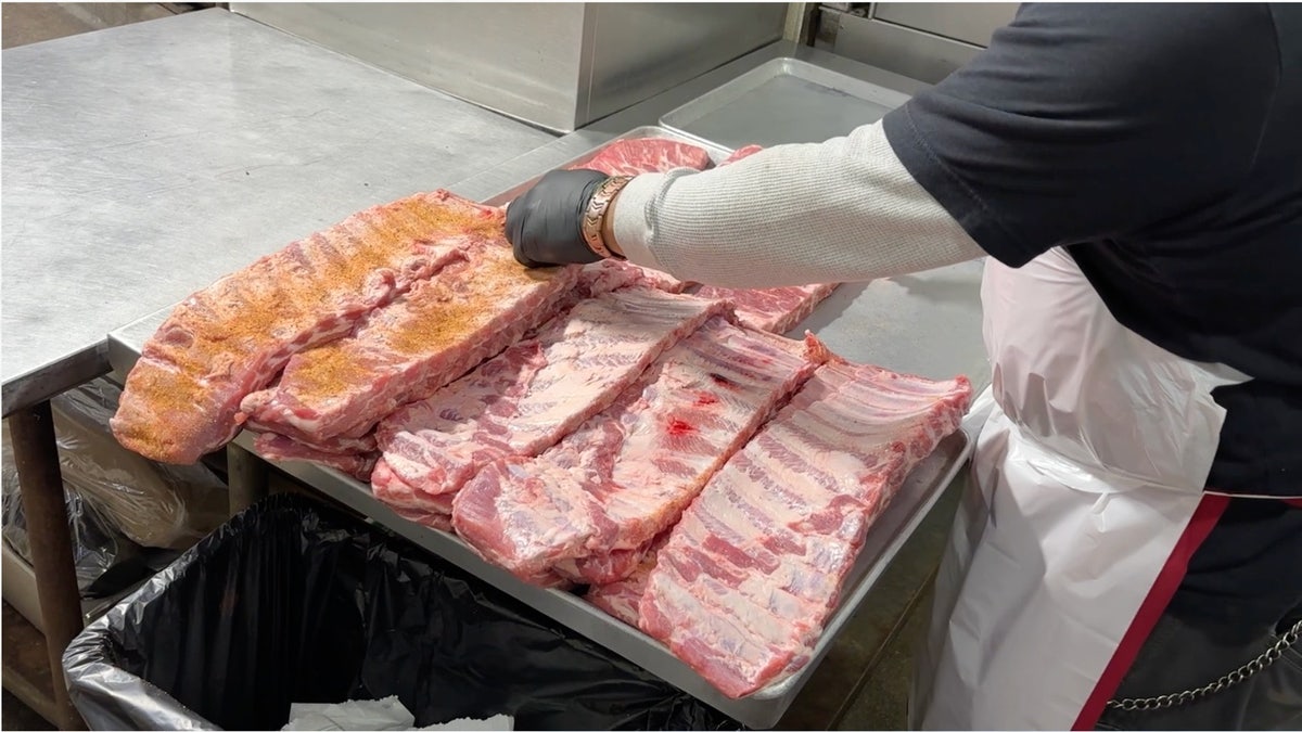 Employee seasoning racks of ribs inside Joe’s Kansas City Bar-B-Que kitchen.