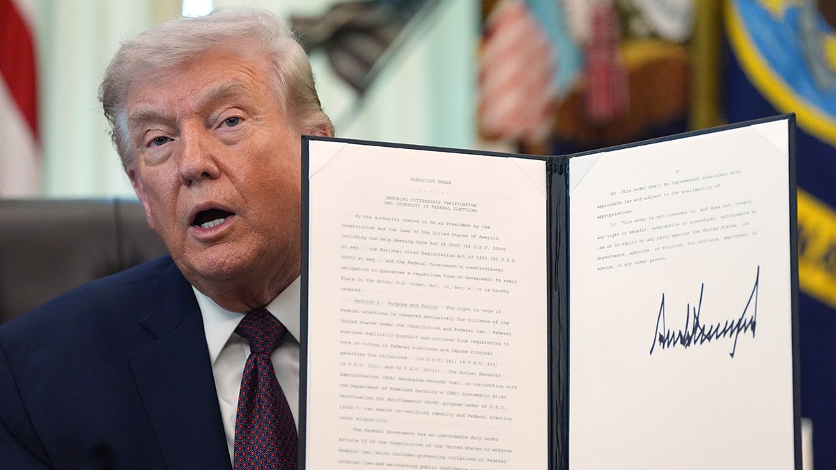 President Donald Trump holding a signed executive order in the Oval Office