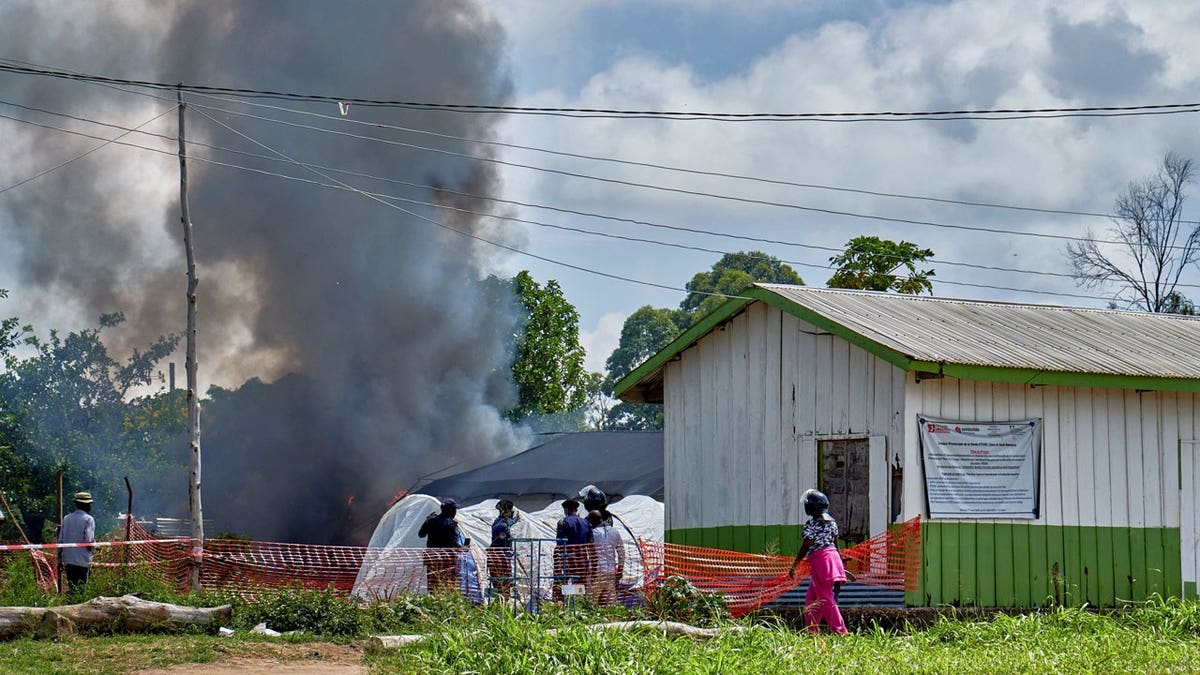 Congolese police personnel and civilians stand near the burning Ebola treatment center