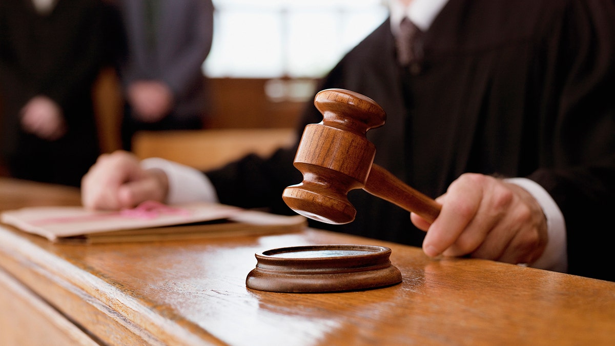 Close-up of a judge holding a wooden gavel above a sound block in a courtroom.