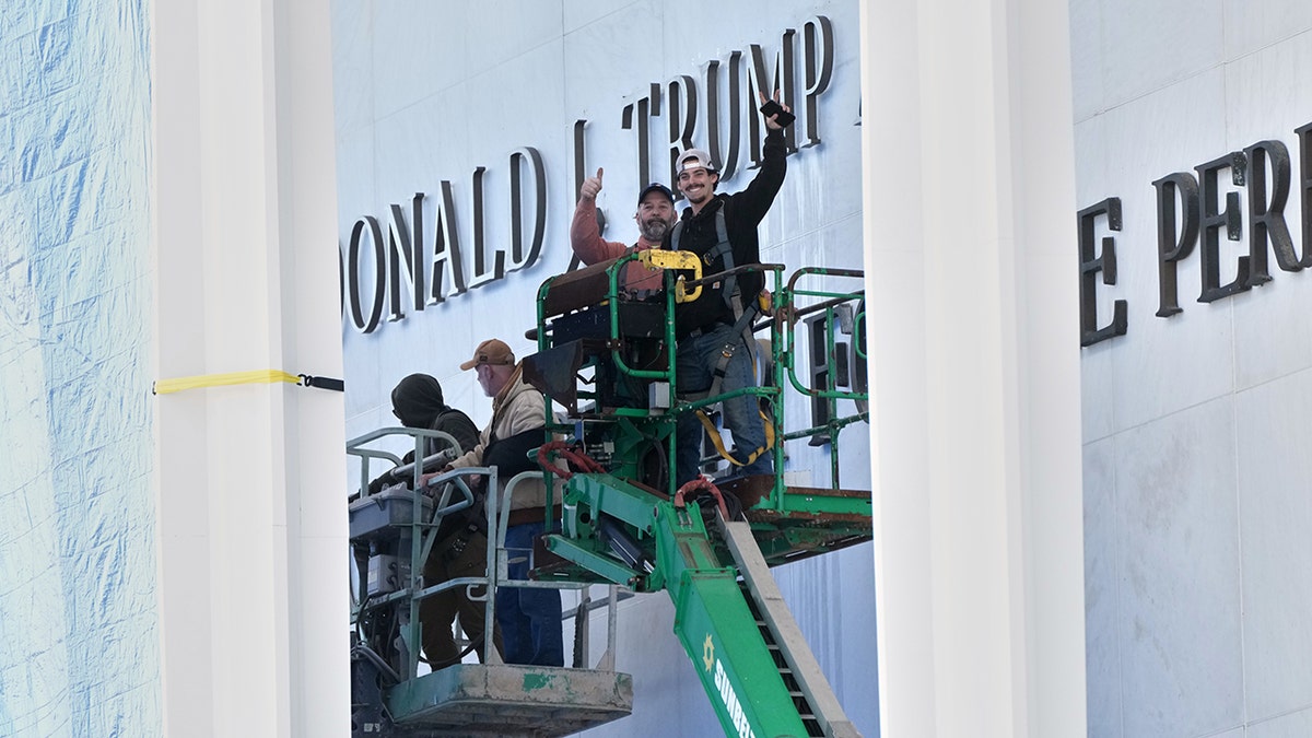 Workers installing Donald J. Trump signage above Kennedy Center sign in Washington