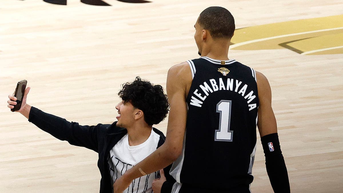 Fan taking a selfie with Victor Wembanyama on basketball court